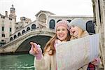 Modern family taking a winter break to enjoy inspirational adventure in Venice, Italy. Mother with map pointing daughter on something while standing in front of Ponte di Rialto