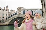 Modern family taking a winter break to enjoy inspirational adventure in Venice, Italy. Happy mother and daughter taking photos while standing in front of Rialto Bridge