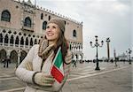 Delightful Venice, Italy can help make the most of your next winter getaway. Smiling young woman tourist with Italian flag standing on St. Mark's Square near Dogi Palace and looking into the distance