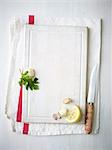 A lemon wedge, garlic cloves and parsley on a white chopping board