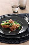 Sausage wrapped in bacon on green beans with pine nuts and spring onions