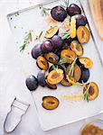 Damsons with rosemary, lemon zest and sugar on a baking tray