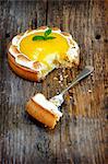 A lemon meringue tartlet on a wooden surface with a bite taken out of it