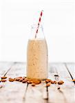 A bottle of almond milk and almonds on a wooden surface