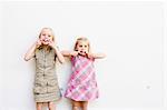 Portrait of two cute sisters pulling faces in front of white wall