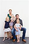 Family portrait of parents and three young daughters in front of white wall