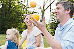 Mature man juggling oranges at family picnic in park
