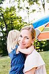 Portrait of mid adult woman and toddler daughter hugging in park