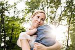 Mid adult woman carrying toddler daughter in sunlit park