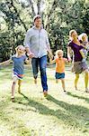 Couple running and holding hands with three  daughters in park