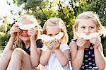 Portrait of three young sisters holding smiling melon in front of face in park