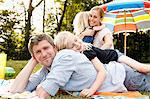 Young daughter lying on top of father at family picnic in park