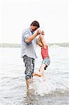 Mature man lifting up daughter from lake Starnberg, Bavaria, Germany