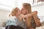 Mid adult woman kissing toddler daughter  on sofa