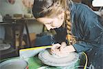 Young woman with plaited hair using pottery wheel