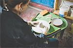 Over shoulder view of young woman sitting using pottery wheel