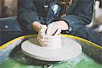 Cropped view of young woman sitting at pottery wheel making clay pot