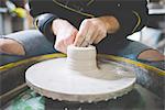 Cropped front view of mid adult man making clay on pottery wheel