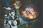 High angle view of young woman using tongs to remove clay pots from fire