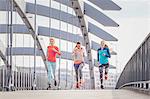 Three female runners running on city footbridge