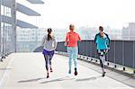 Rear view of three female runners running across city footbridge