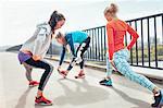 Three female runners doing warm up exercise on footbridge