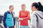 Three female runners coordinating time on city footbridge