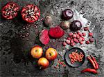 Overhead view of halved red fruit and vegetables on dark background