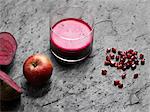 High angle view of purple raw juice, halved beetroot, apple and pomegranate seeds