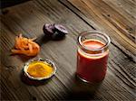 High angle view of orange raw juice in a jar with beetroot, turmeric and grated carrot on wood grain pattern background