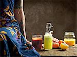 Cropped view of  woman wearing dress sitting on table with raw juices in glass bottle and jars