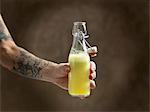 Tattooed womans arm holding raw juice in glass bottle