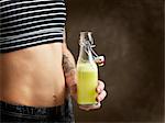 Cropped view of womans bare midriff, holding raw juice in glass bottle