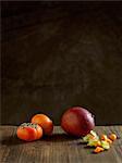 Whole mango and persimmons on wood table against dark background