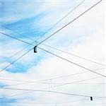 Low angle view of blue sky and street lights with criss crossed wires