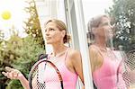 Mature female tennis player leaning against patio door