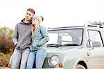 Romantic young couple leaning against car at beach