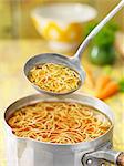 Saucepan and ladle of beef noodle soup with carrots, herbs and stock