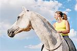 Low angle view of woman riding grey horse bareback against blue sky