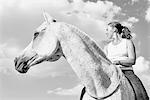 B&W portrait of woman riding grey horse against sky
