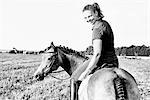 B&W portrait of woman riding horse in field and looking over her shoulder