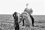 B&W image of woman chatting with man riding grey horse in field