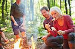 Multi-generation family roasting marshmallows at campfire in forest