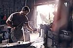 Blacksmith using blow torch in forge