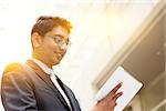 Portrait of Asian Indian business man using touch screen tablet computer, outside modern office building block, beautiful golden sunlight at background.