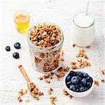 Healthy breakfast. Fresh granola, muesli in a glass jar with yogurt, fresh blueberry and honey on a white wooden background