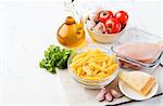 Italian food ingredients: pasta, tomatoes, herbs, chicken and spices on wooden background