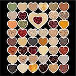 Large dried superfood collection in heart shaped porcelain china bowls forming an abstract background  over black background. High in minerals, vitamins and antioxidants.