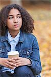 Beautiful mixed race African American girl teenager female young woman drinking takeaway coffee outside sitting in a park in autumn or fall looking sad depressed or thoughtful