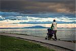 Mother with Baby Stroller Walking by the Sea and Enjoying Beautiful Seascape in Evening. Happy Parenting and Healthy Lifestyle Concept. Copy Space.